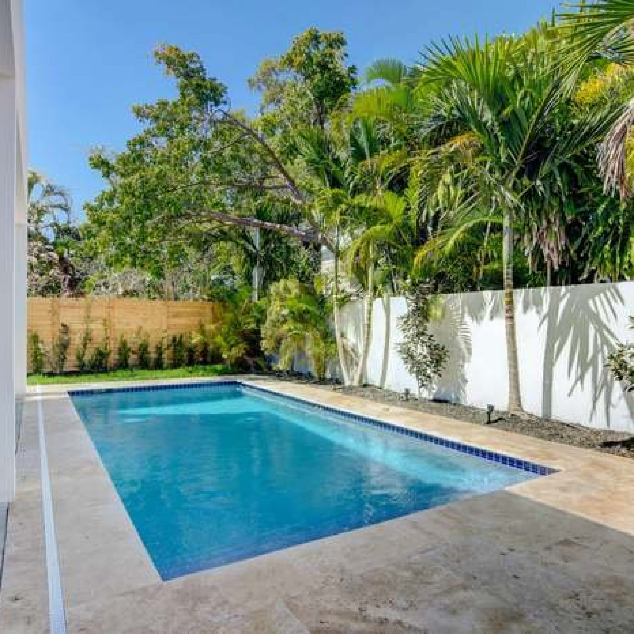 Rectangular pool with travertine coping beside a covered lanai with potted plants