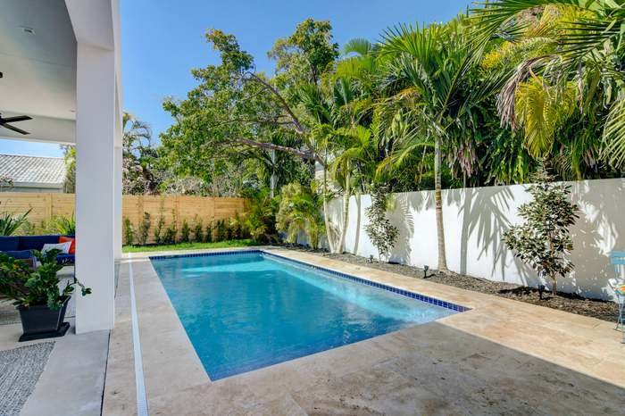 Rectangular pool with travertine coping beside a covered lanai with potted plants