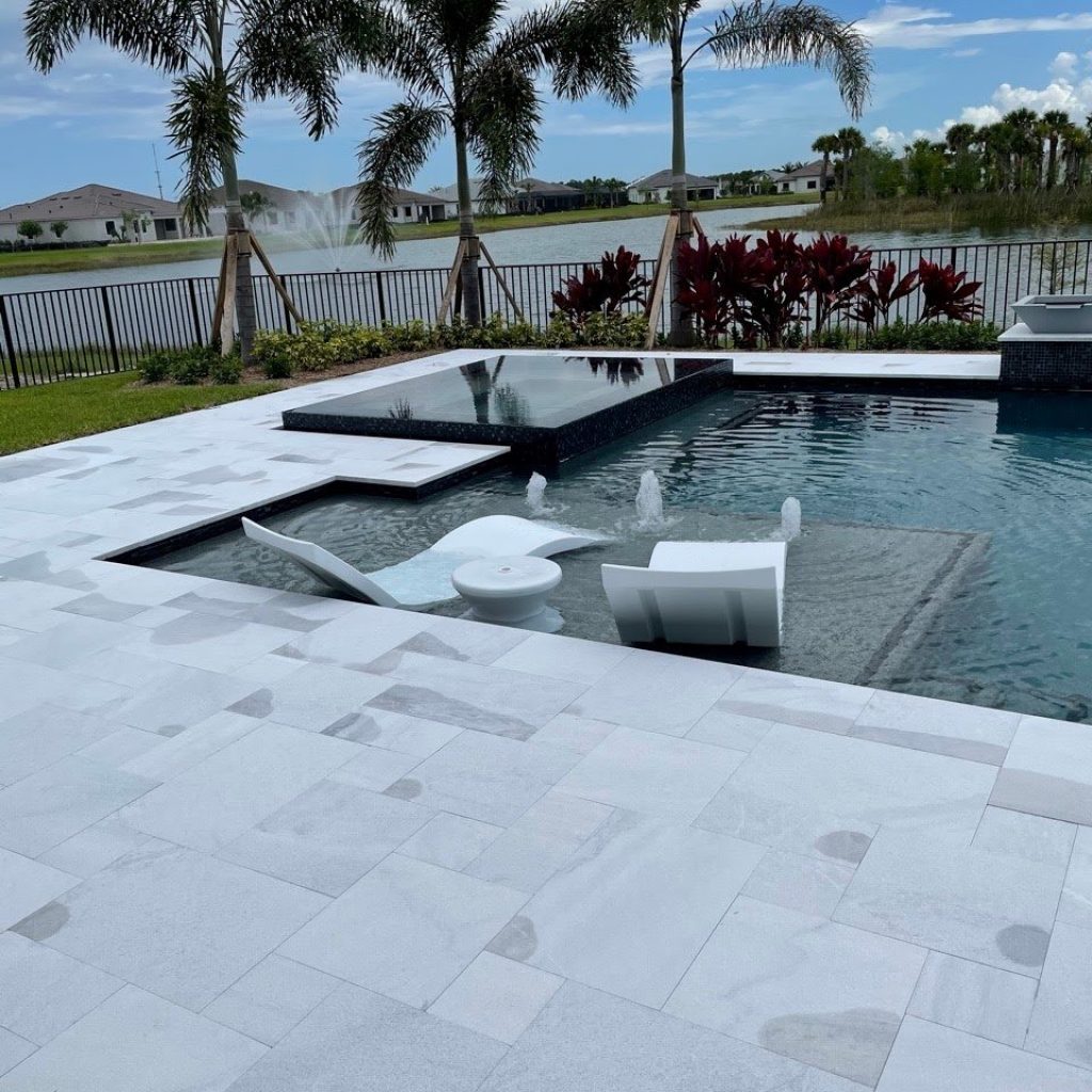 Modern pool with in-pool sun shelf loungers and a raised spa surrounded by a white travertine deck