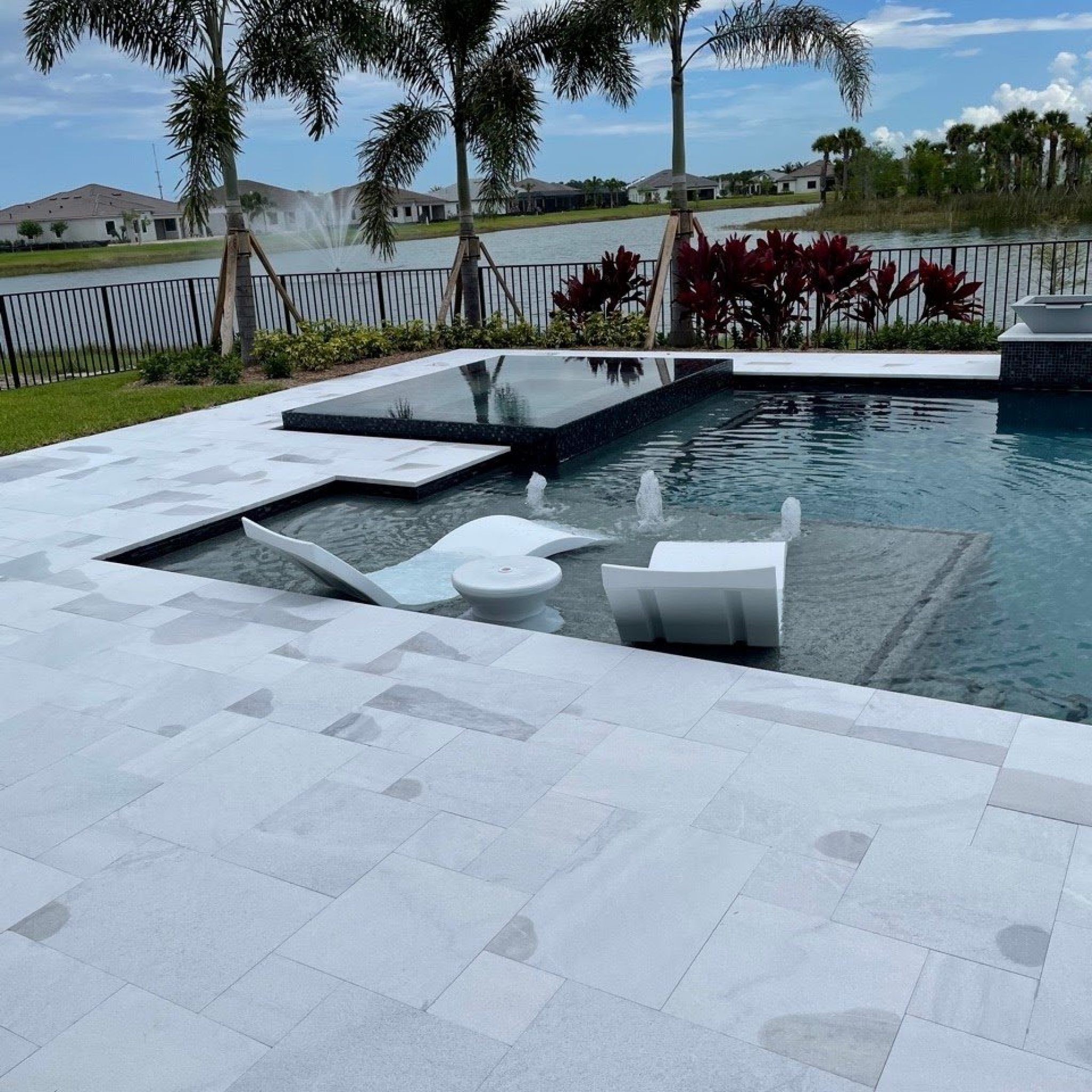 Modern pool with in-pool sun shelf loungers and a raised spa surrounded by a white travertine deck