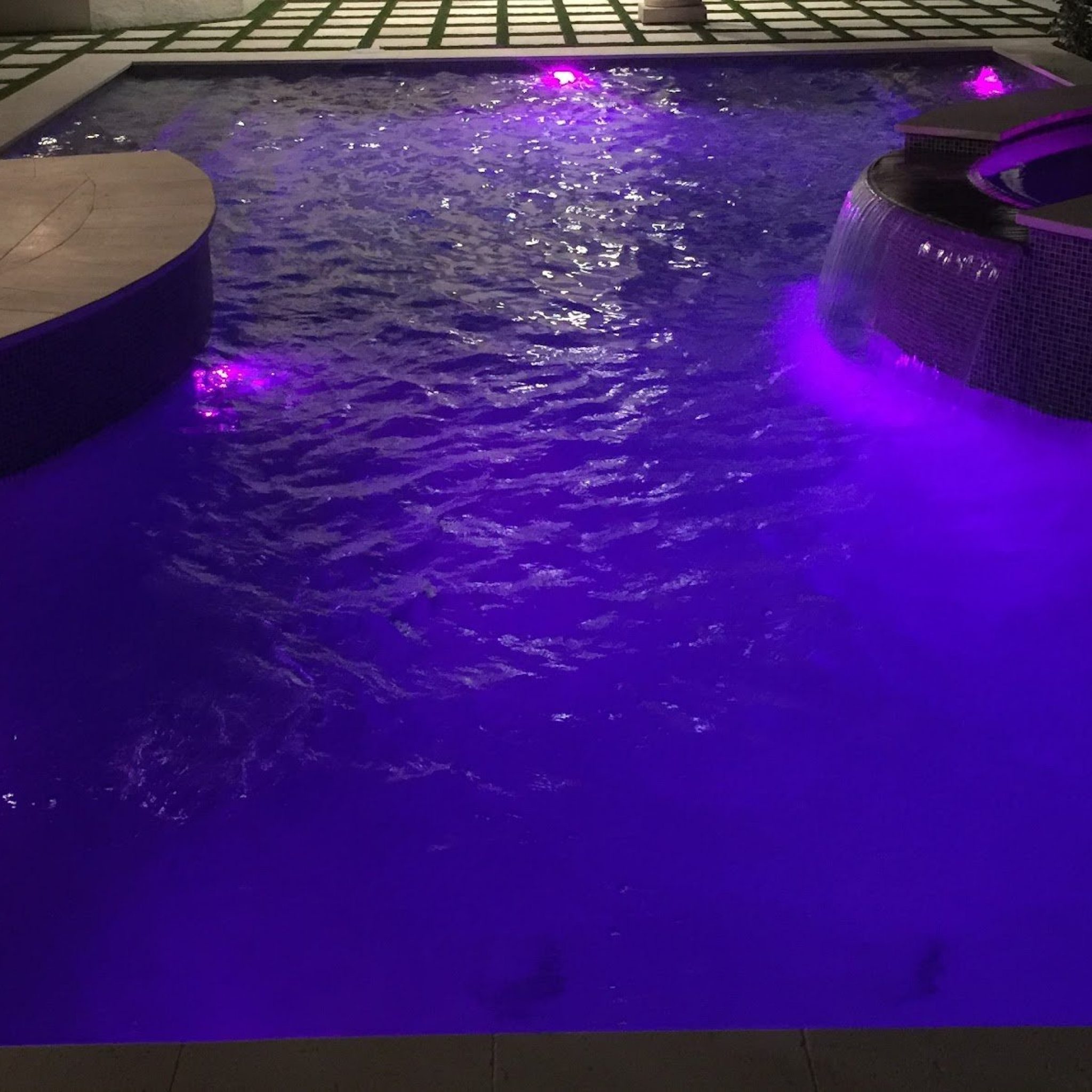 Pool and raised spa glowing with purple LED lighting at night