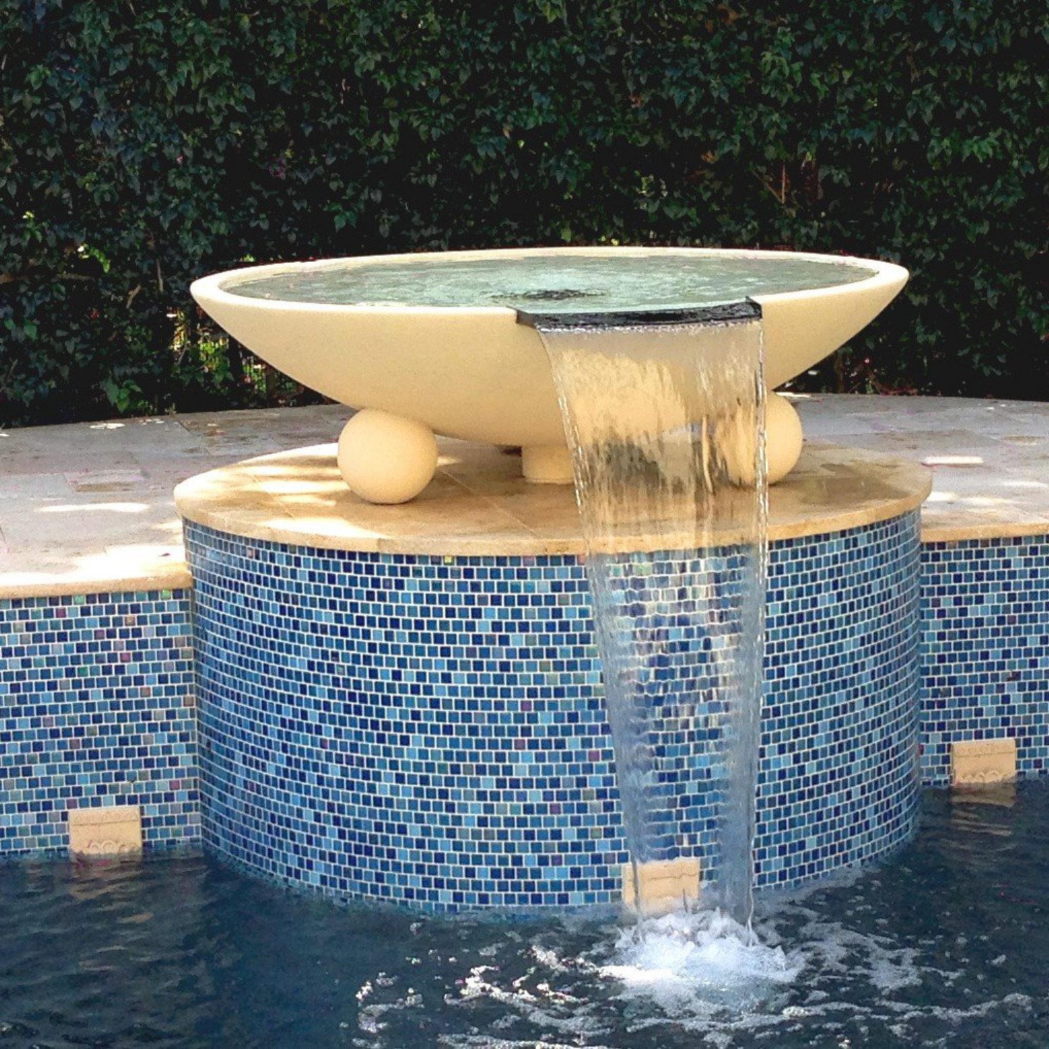 Large pool water bowl spilling over a blue glass-tile pedestal into the pool