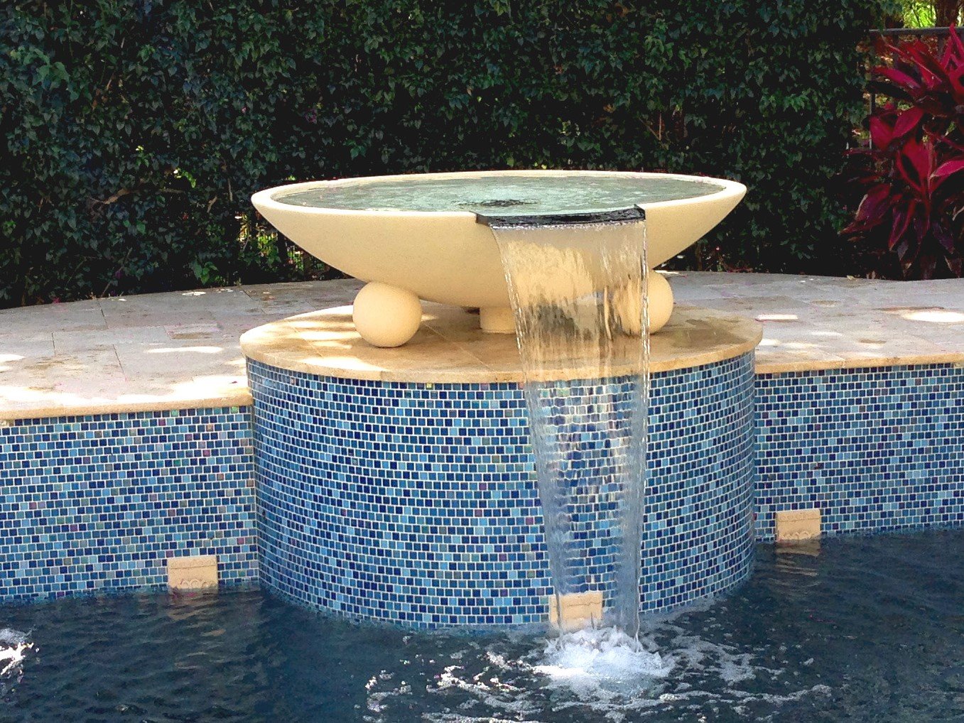 Large pool water bowl spilling over a blue glass-tile pedestal into the pool