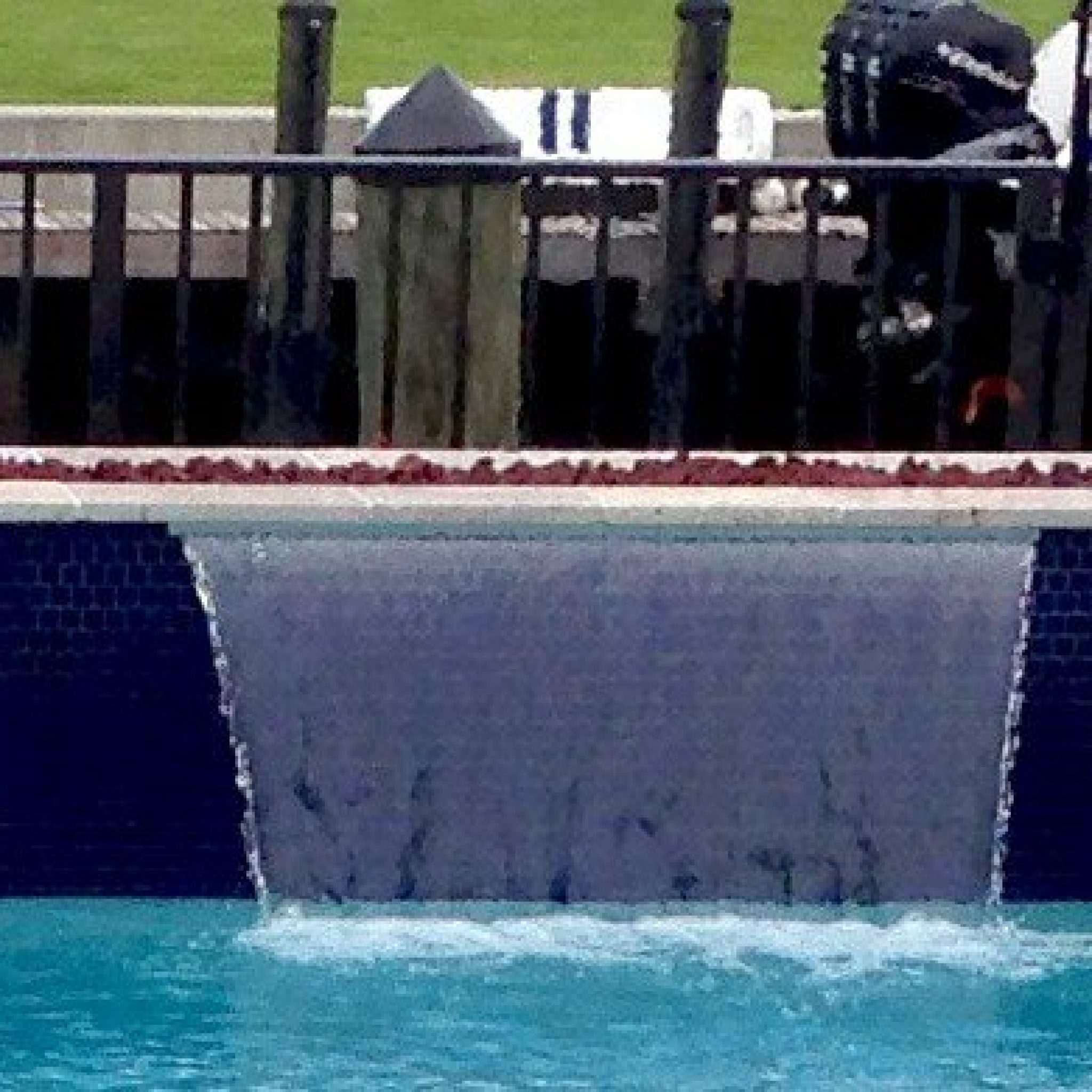Raised beam with a linear fire feature above a sheer descent waterfall into a blue tile pool