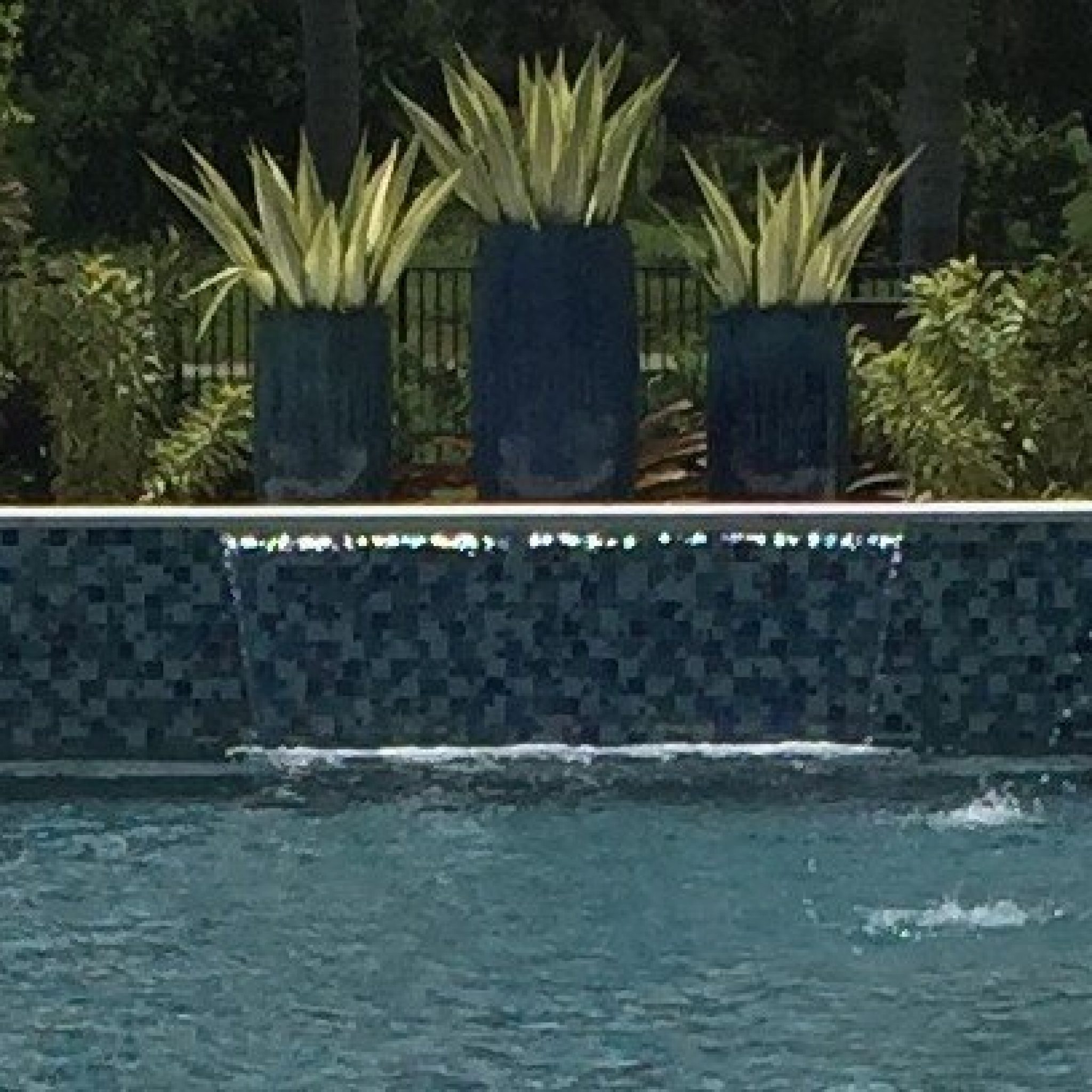 Raised tile beam with sheer descent waterfalls and planter pots along a pool