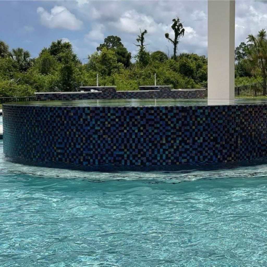 Raised spa wrapped in blue glass mosaic tile spilling over into the pool