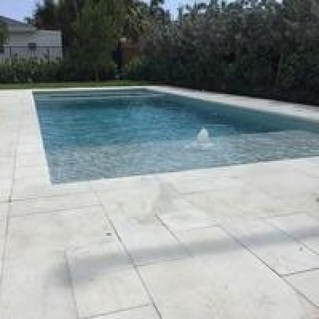 Rectangular pool with sun shelf bubblers and a white travertine deck