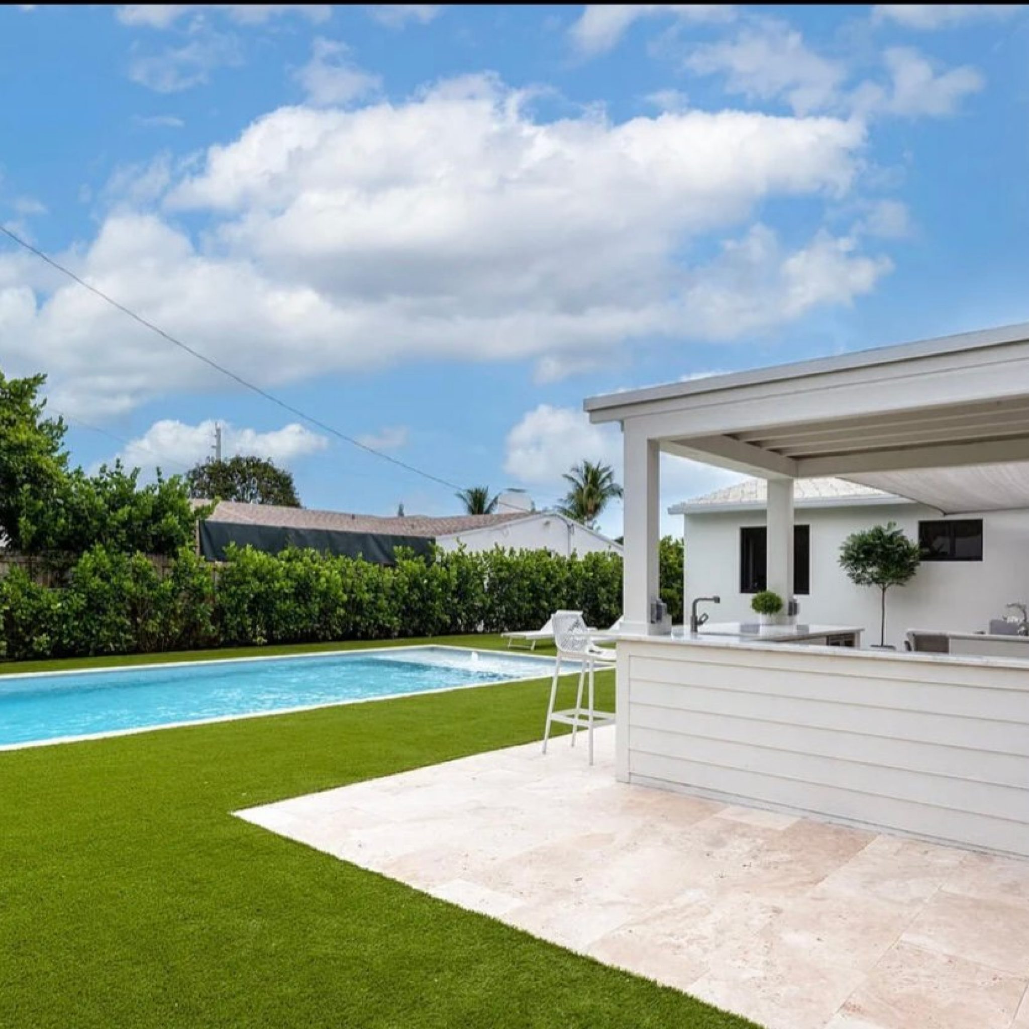 Rectangular pool with travertine deck beside a covered outdoor living patio and summer kitchen