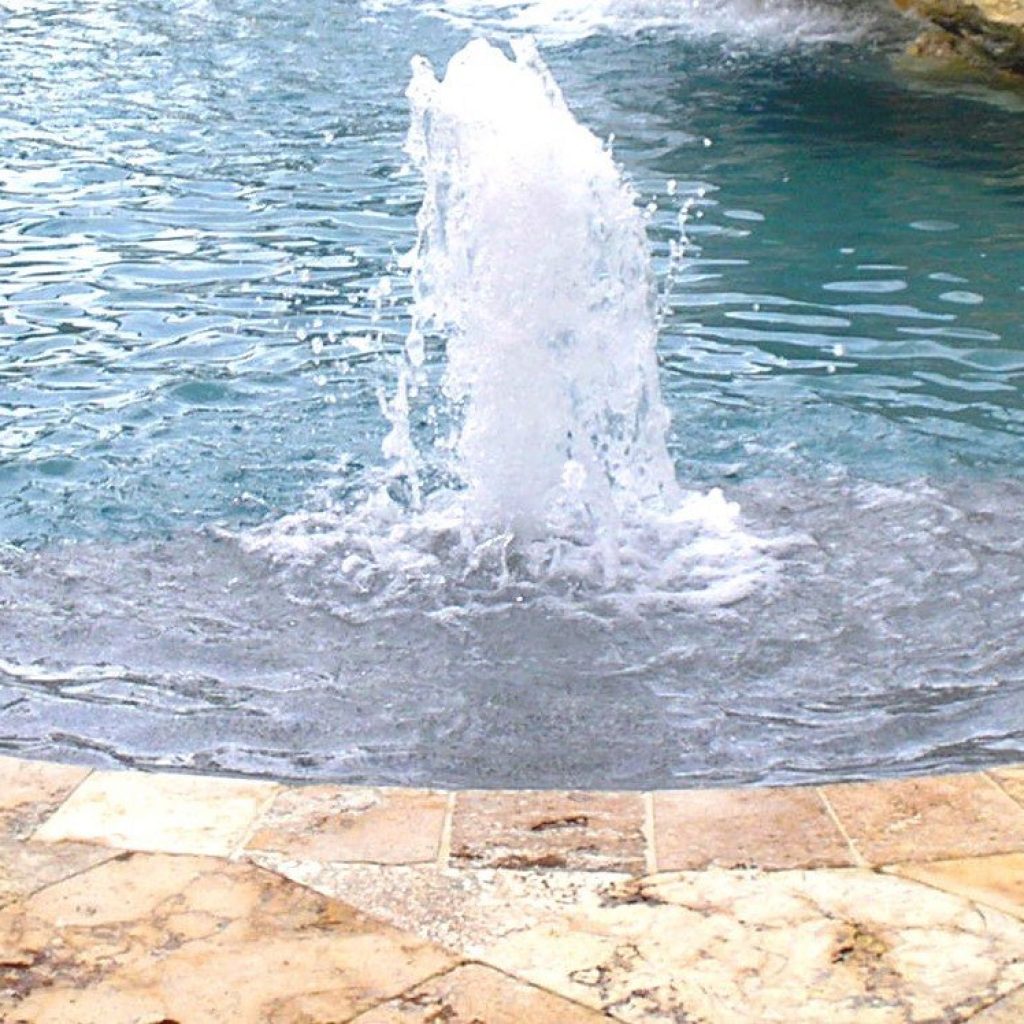 Bubbler fountain spraying water on a pool sun shelf with travertine coping