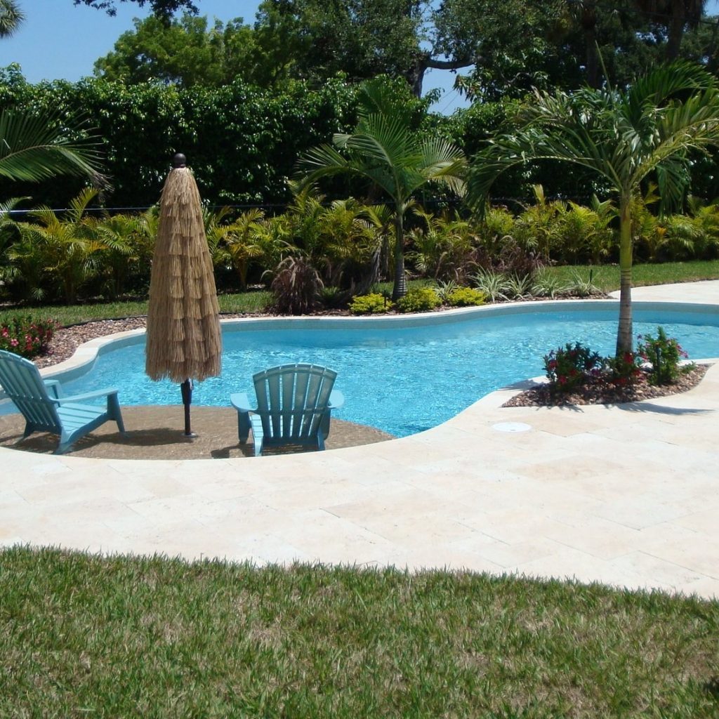 Freeform pool in Super Blue finish with a Mojave Beige sun shelf, umbrella and lounge chairs