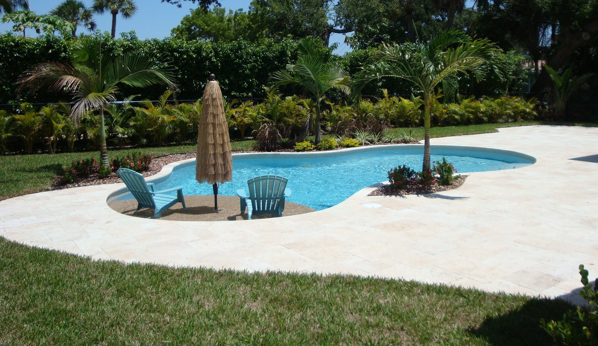 Freeform pool in Super Blue finish with a Mojave Beige sun shelf, umbrella and lounge chairs
